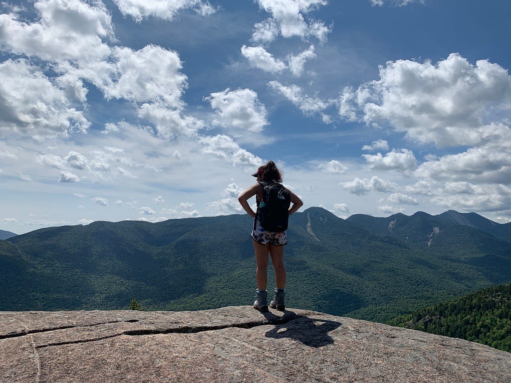 A woman standing on top of a mountain, looking out towards more mountains.