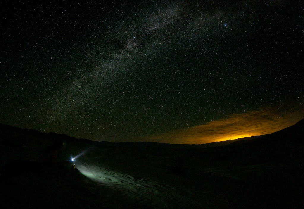 A headlamp beams up into the night sky with the Milk Way arcing overhead.