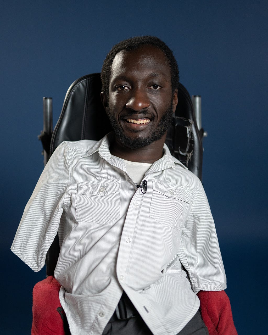A smiling Black man sits in his wheelchair in front of a blue background.