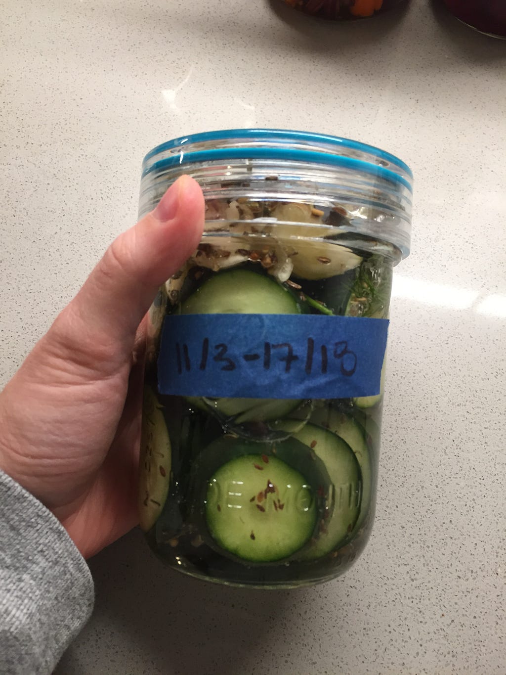 A small wide-mouth jar filled with cucumber slices and packed with salt water.