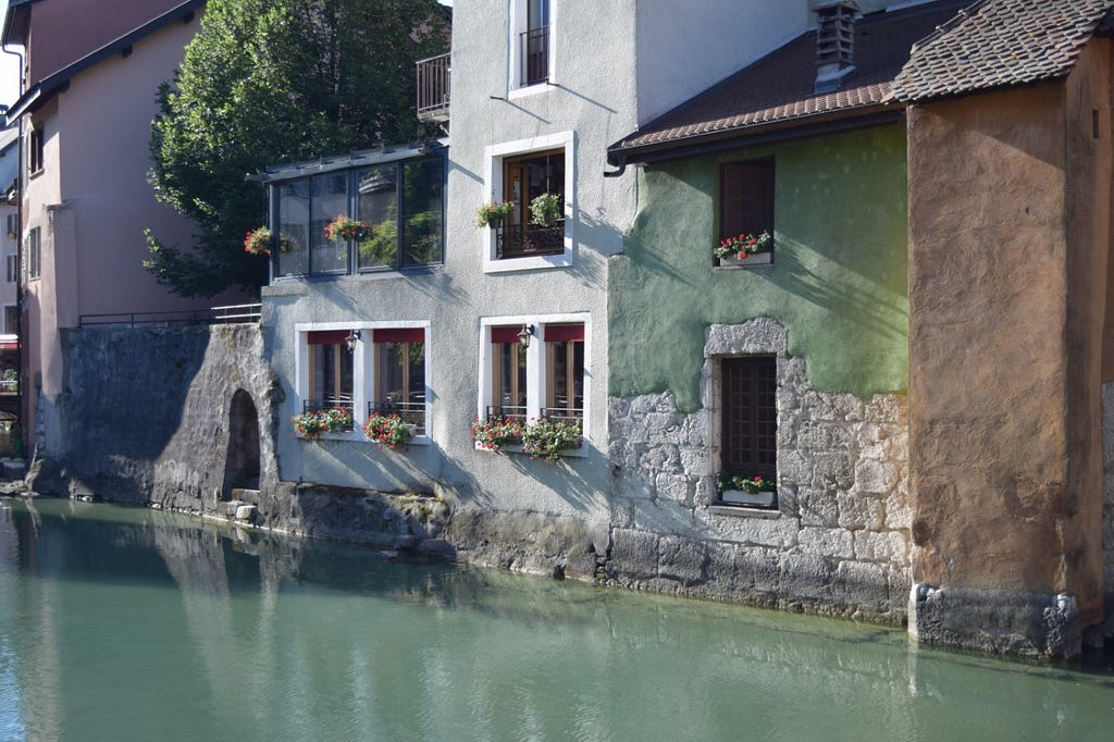A green building and an orange building next to the canal that runs through Annecy’s old town.