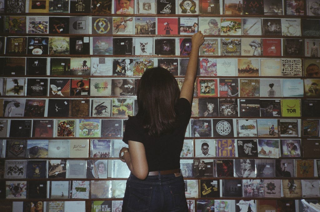 Woman reaching up to grab a CD from a wall of them.