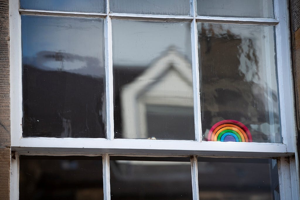 A small rainbow made from plasticine sits behind a large white-framed window
