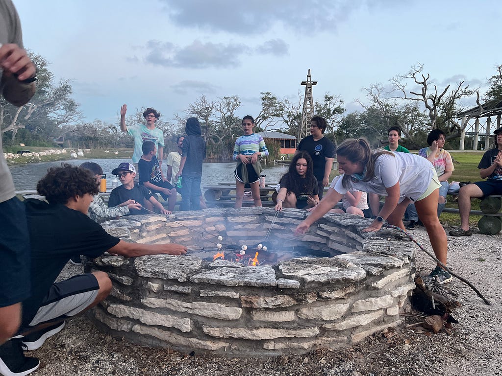 Amelia and campers gather around the campfire to make smores