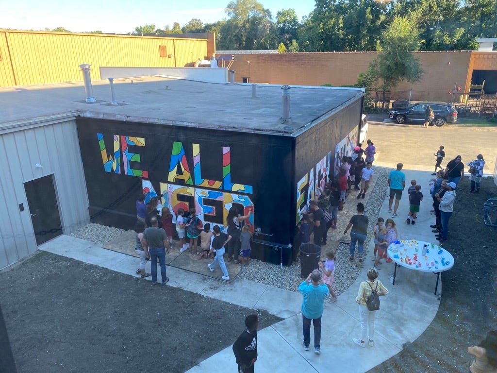 People working on a mural that says “we all need each other”