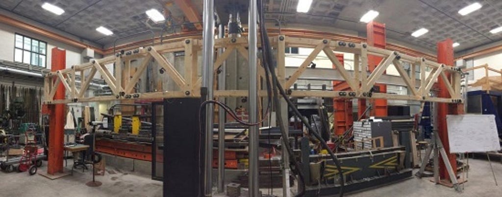A wooden truss in a laboratory surrounded by testing equipment.