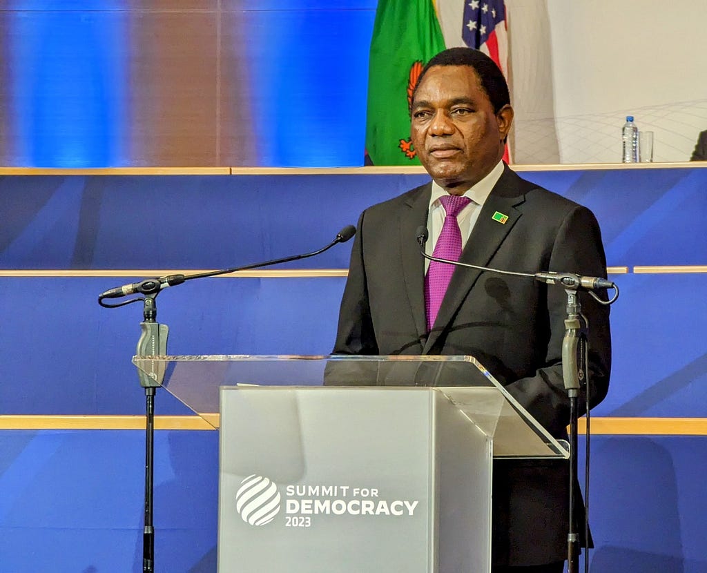 The president of Zambia speaks into two microphones behind a podium that reads “Summit for Democracy 2023.”