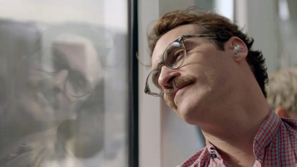 A still from the movie ‘Her,’ where the protagonist, Theodore, smiles gently while looking out a window, listening to his AI companion through a wireless earbud.