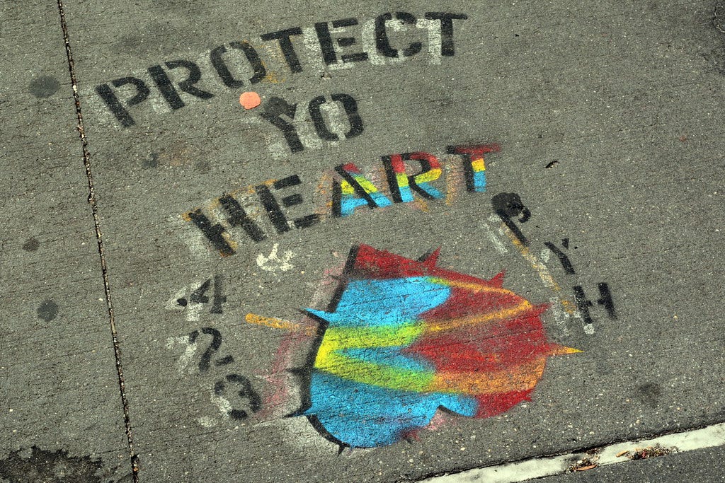Graffiti on a New York sidewalk. The words say “Protect Yo Heart” with the last three letters of “Heart” emblazoned in different colors so that the message also reads “Protect Yo Art”. Beneath the words is an upsidedown heart in red, blue and yellow. To the left of the drawing are the numbers 423, and to the right the letters PYH