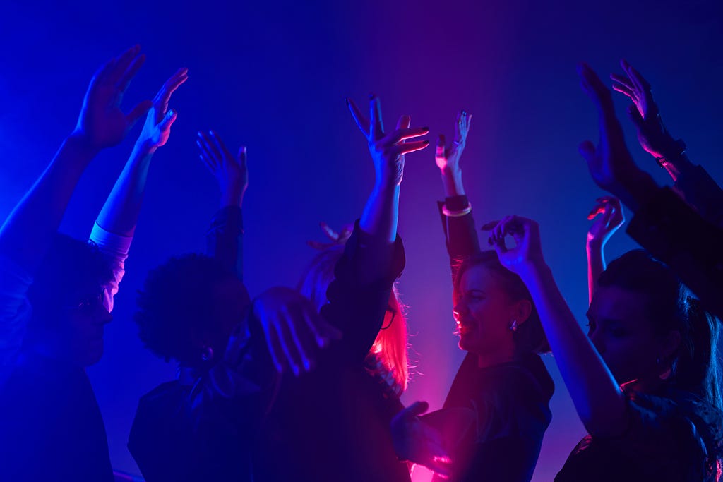 group soaked in neon lighting raising their hands to the sky