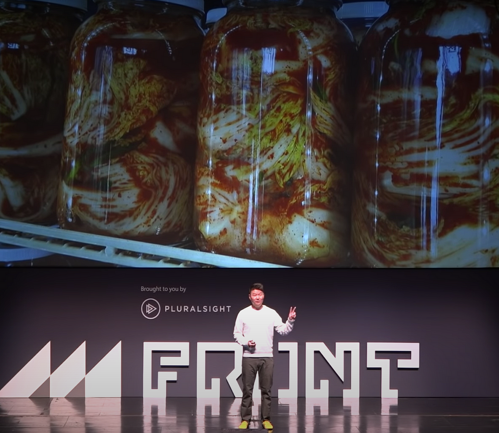 Frank Yoo on stage with a photograph of jars containing kimchi in the background