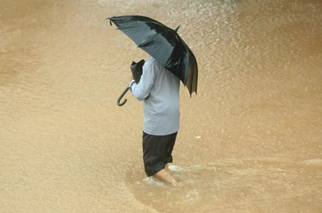 Man wading the waters carrying an umbrella during a flood