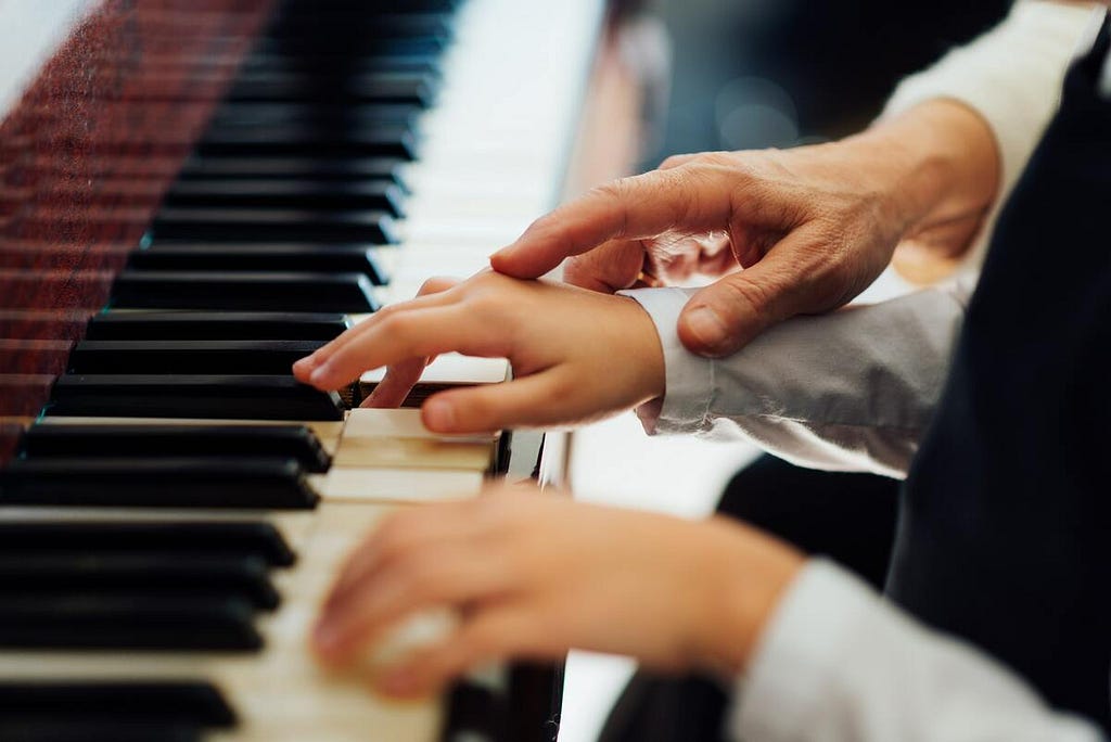 Experienced hand of old music teacher helps child student play the piano.