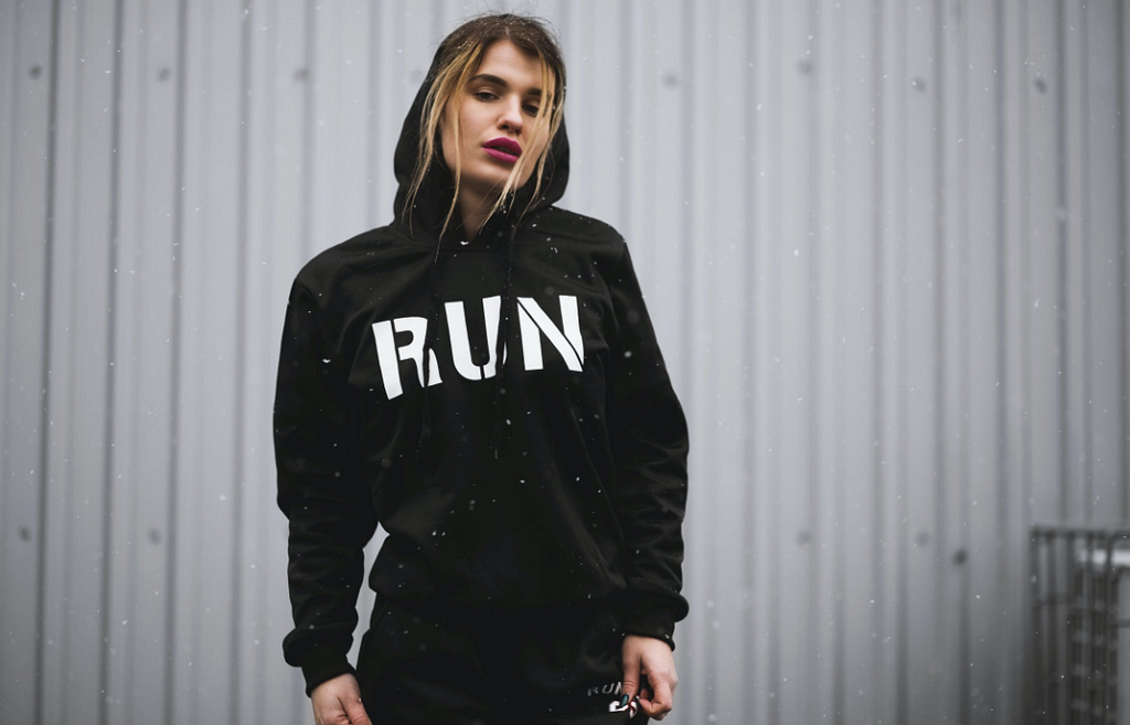A fatigued woman wearing black hoodie, with the word “RUN” emblazoned across her chest.