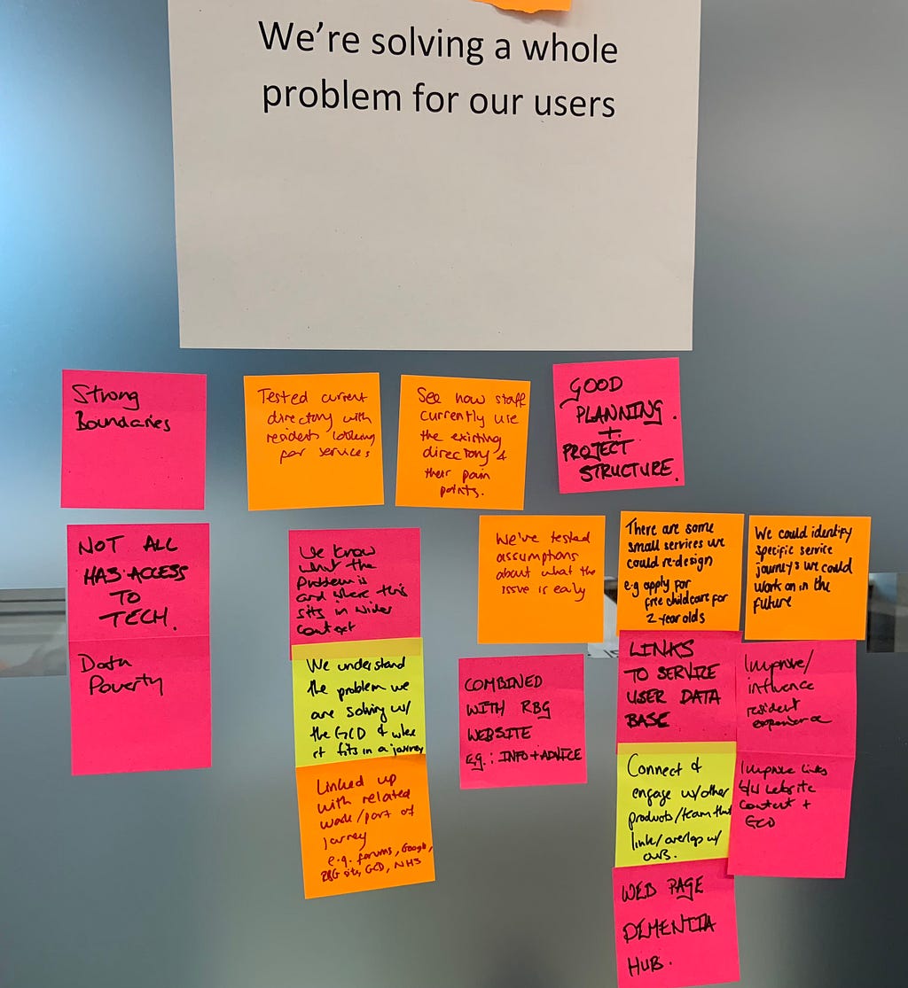 Wall with the service standard ‘We’re solving a whole problem for our users’ with sticky notes surrounding it.