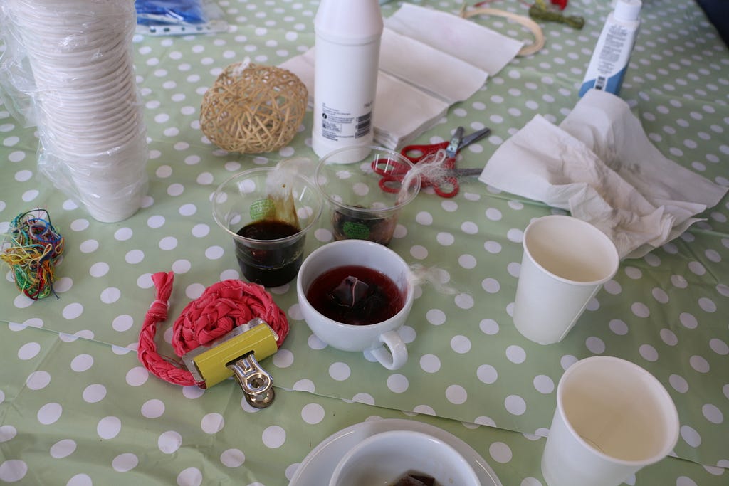A tea cup with a red herbal tea in it, as well as some empty cups and some yarn sit on a table