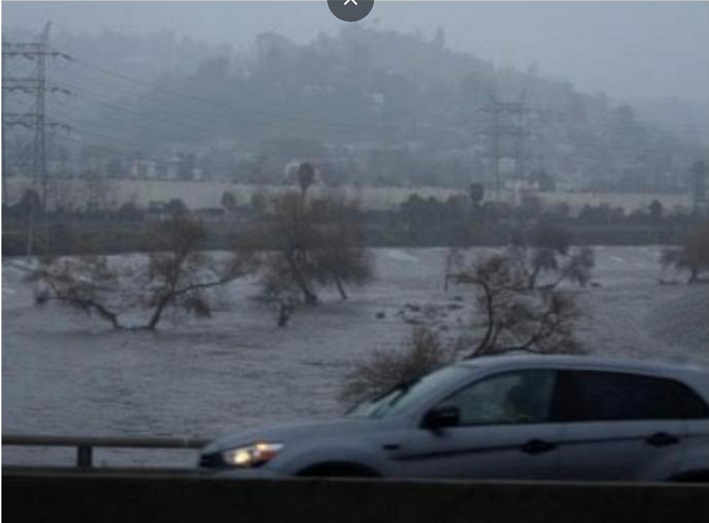 Photo of a car going by the Whittier Narrows dam, that is almost overflowing.