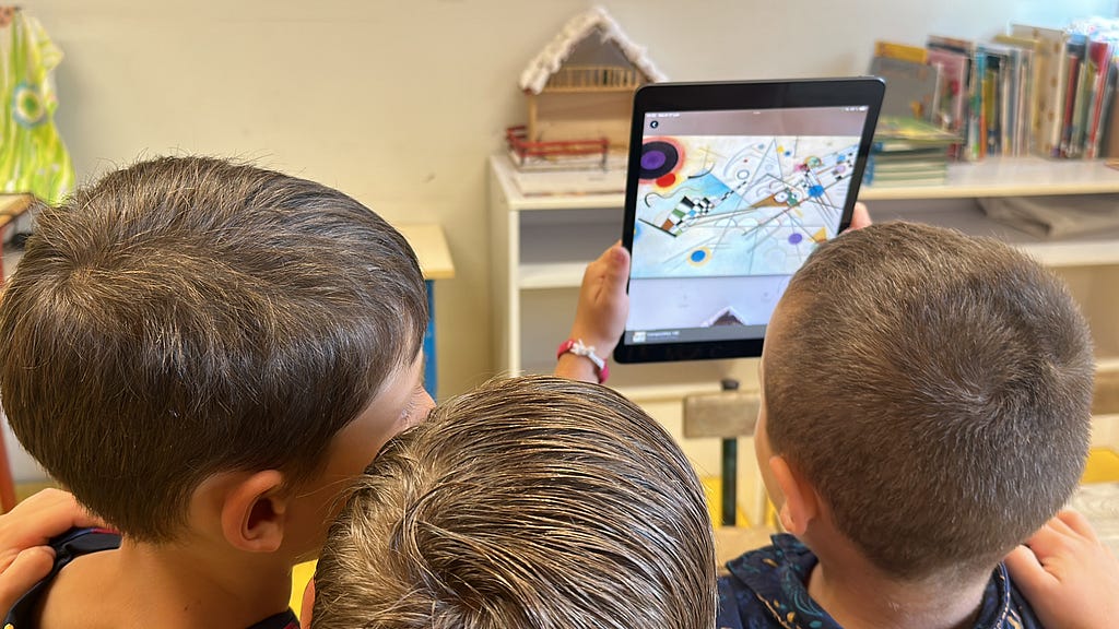 Three children seen from behind, looking at a work of art by Kandinsky in augmented reality using an iPad.