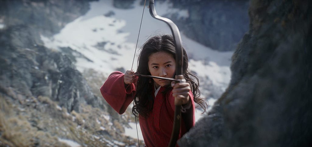 Mulan, from the live-action 2020 movie, is standing with her bow and arrow, ready to fire at the enemy.