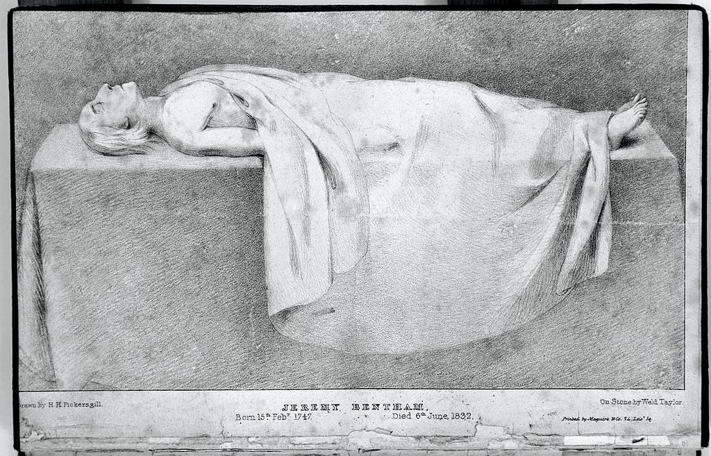 A monochrome plate showing the body of Jeremy Bentham, draped with a white sheet. He looks peaceful and seems to be pre-autopsy. The image is cold but not gory.