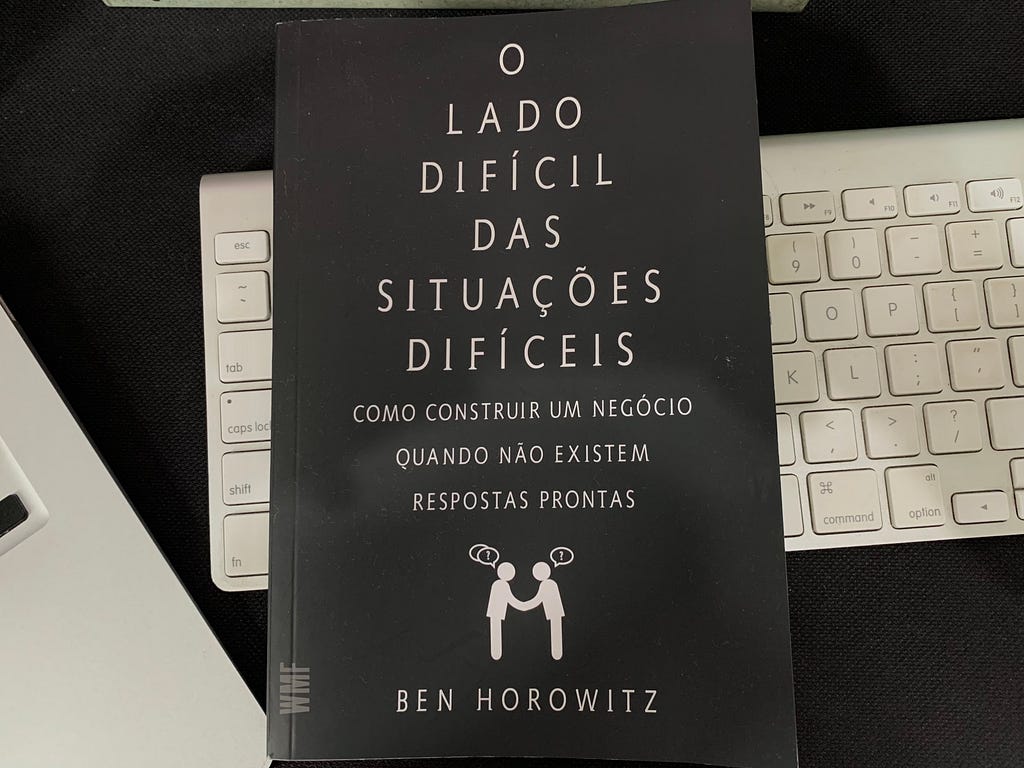 Foto do livro “O lado difícil das situações difíceis” de Ben Horowitz em cima de um teclado de computador branco