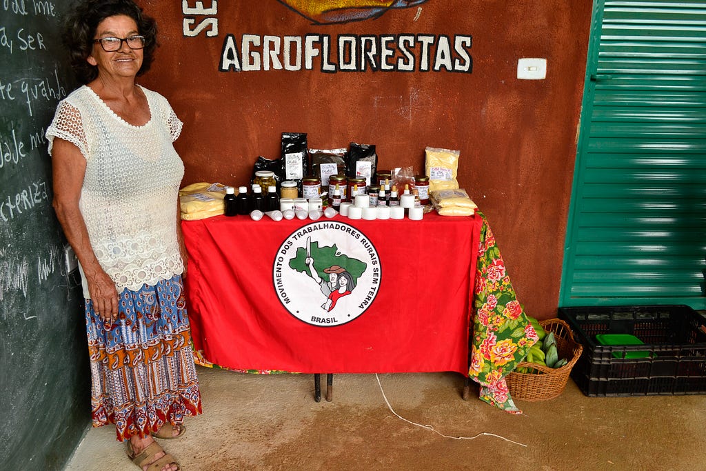 Dona Ricarda exibe, numa mesa com a bandeira do MST, o café Guaíi, fitoterápicos e outros produtos do assentamento.
