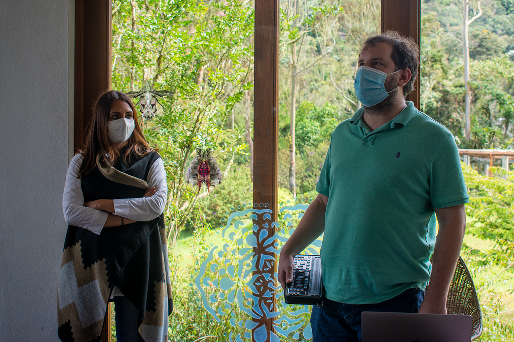 Juan Pablo stands next to one of his students in during a workshop about building an inclusive birdwatching trail next to a floor-to-ceiling wall of glass.