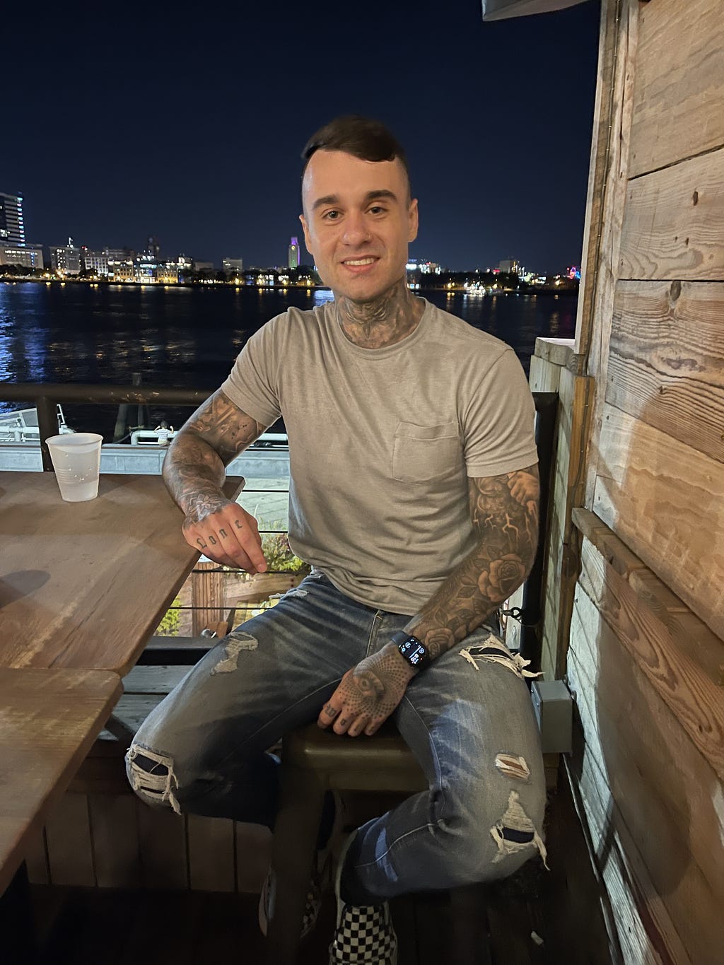 Founder of Conefluence, Justin Grome sitting on a table with a view of sea and cityscape behind him