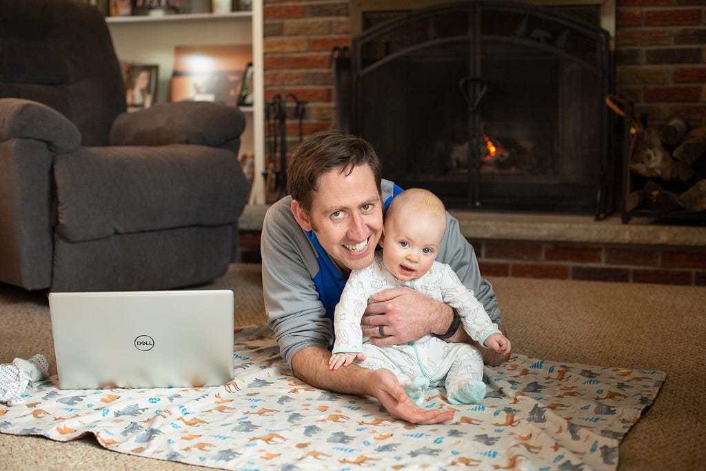 father and son sitting on the floor in front of a fire with a laptop open