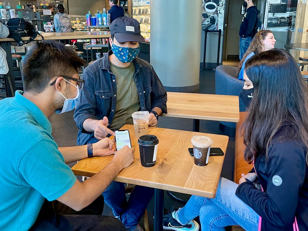 Three students conducting a usability test on a mobile phone in a cafe