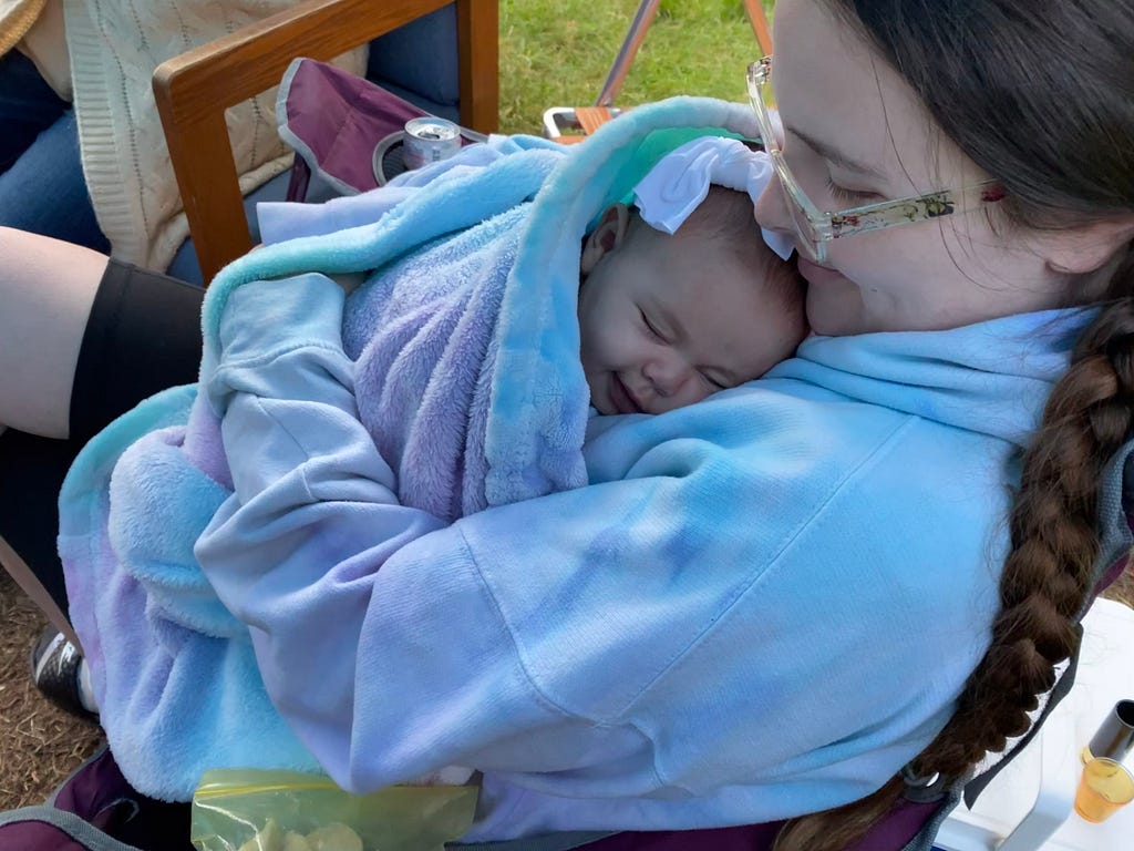 A mother smiling looking down at a smiling sleeping babe wrapped in a blanket.