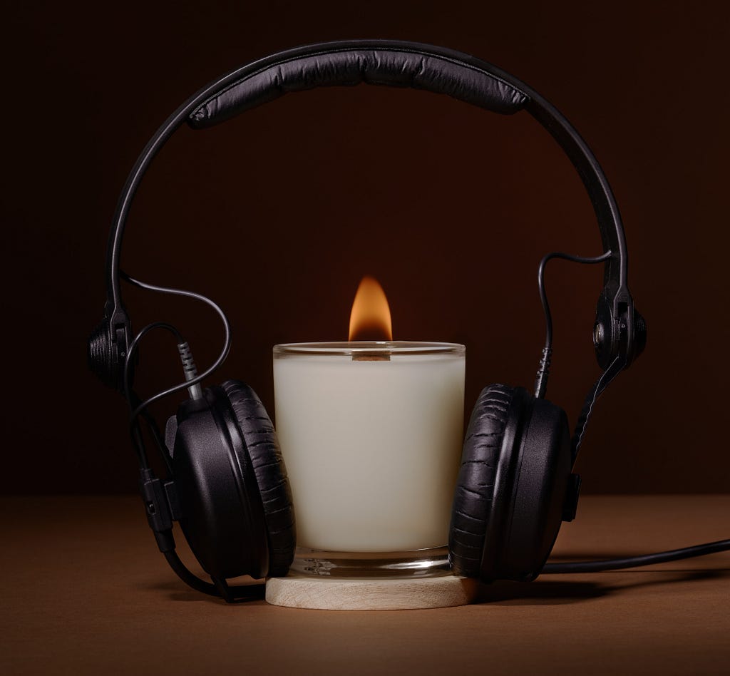 Headphones positioned on a small lit candle, as if the candle were listening to something that ignited the wick.