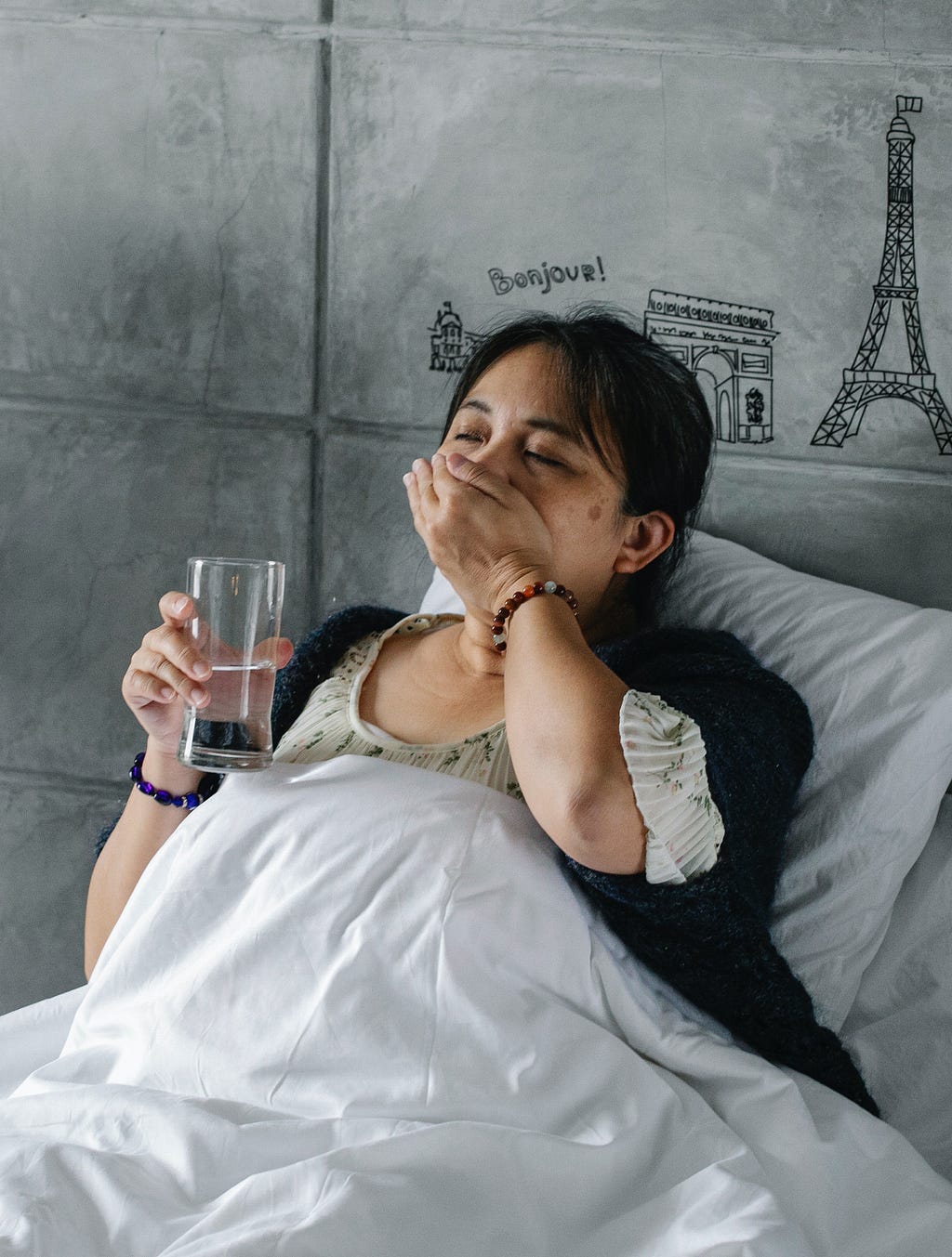a woman laying on a bed while swallowing a pill and holding a glass of water