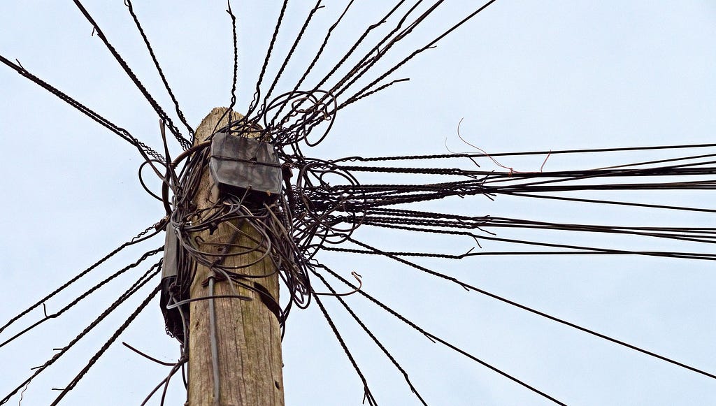 Image of a telephone poll with too many wires connected.