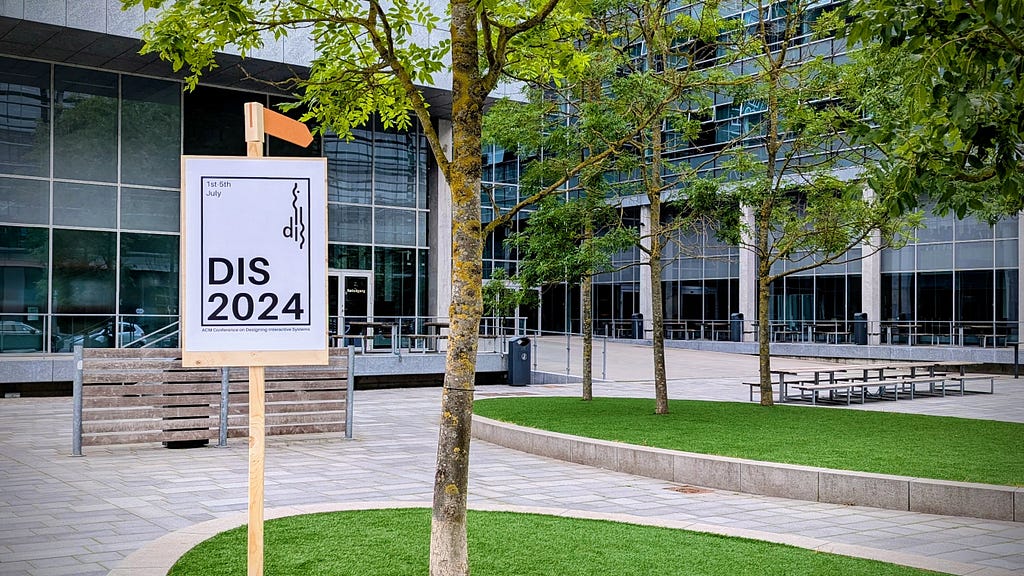 Photo of the conference entrance, showing a DIS 2024 sign, some trees, and the building and entrance.