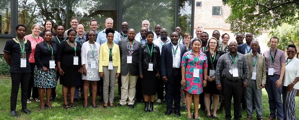 Colleagues from FoSTA Health gather to pose for a photograph outdoors. They are standing on the grass in front of a building with a glass wall.