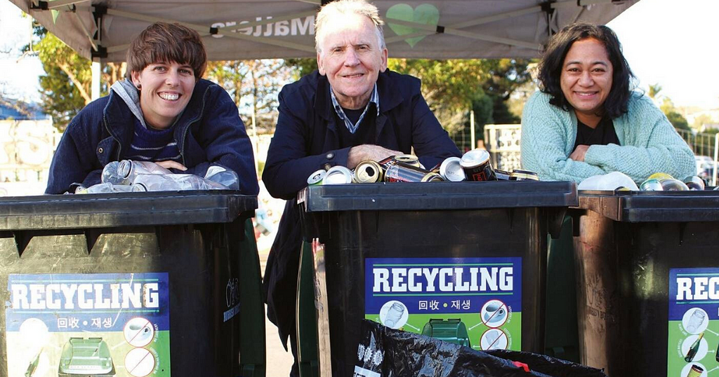 Holly and Warren with Ina Patisolo from Eco Matters leaning on full recycle bins at a community bottle drive