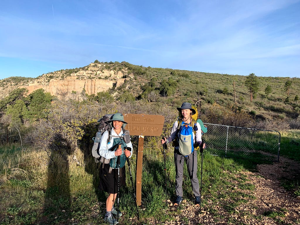 two women at a trailhead wearing backpacks and frontpacks