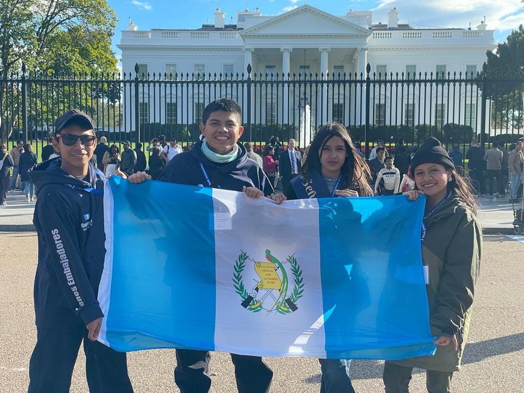Four young adults pose with the Guatemala flag in front of the White House in Washington, DC.