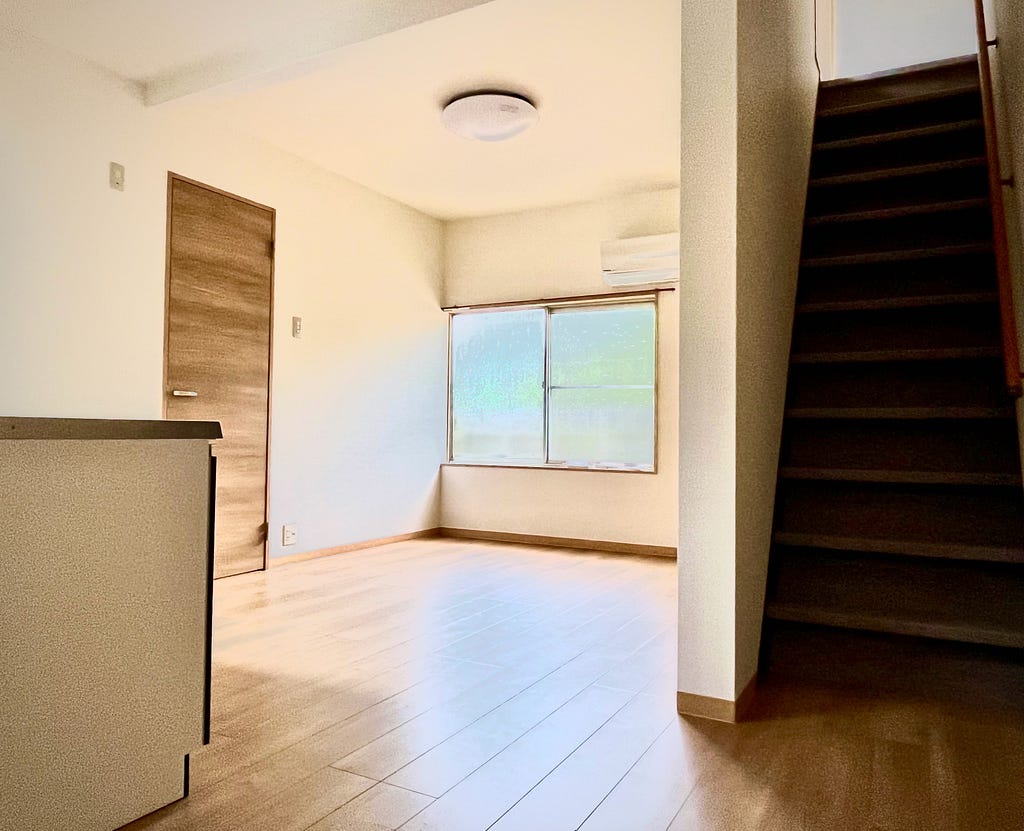 A sunlit, empty living/dining space with a steep staircase to the right