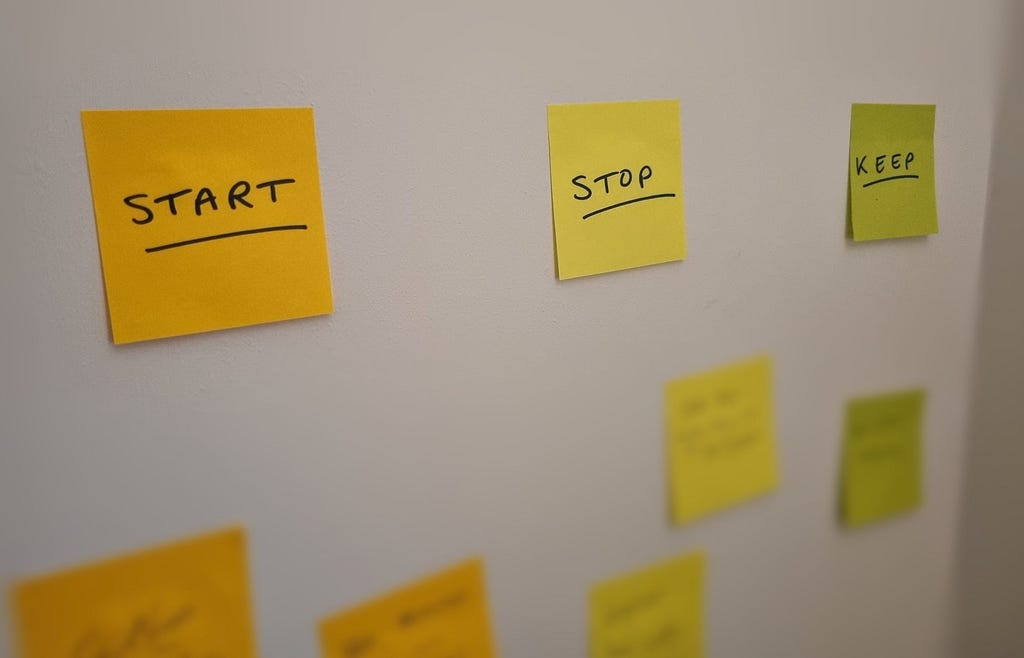 Headers of Start, Stop and Keep, with blurred sticky notes underneath each of them, on a wall