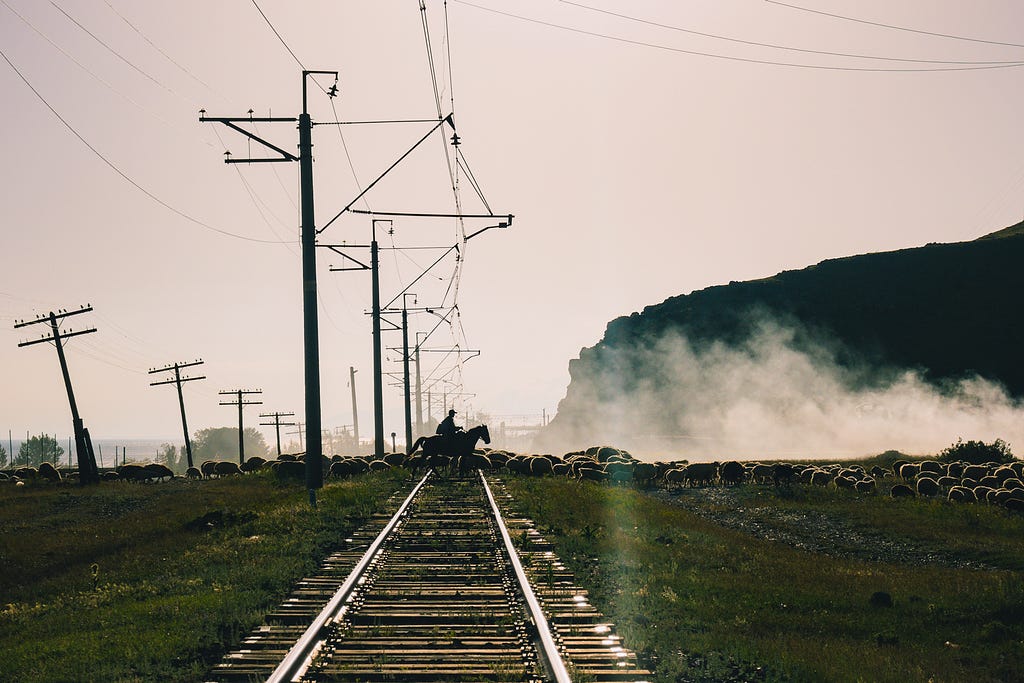 A shepherd riding a horse crossing a railway near Shorzha, Armenia