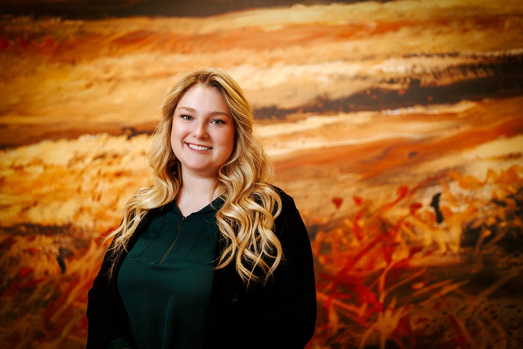 Delaney smiles for a photo in front of a mural depicting grasses