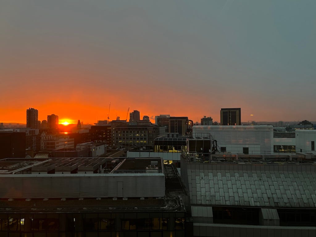 An orange sun rises over building rooftops in London.