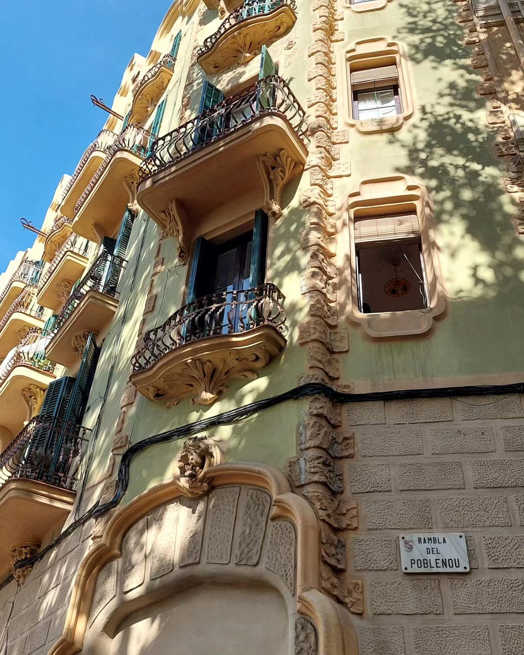 A green building with modernist architectural details on Rambla del Poblenou during a walk on a sunny Sunday.