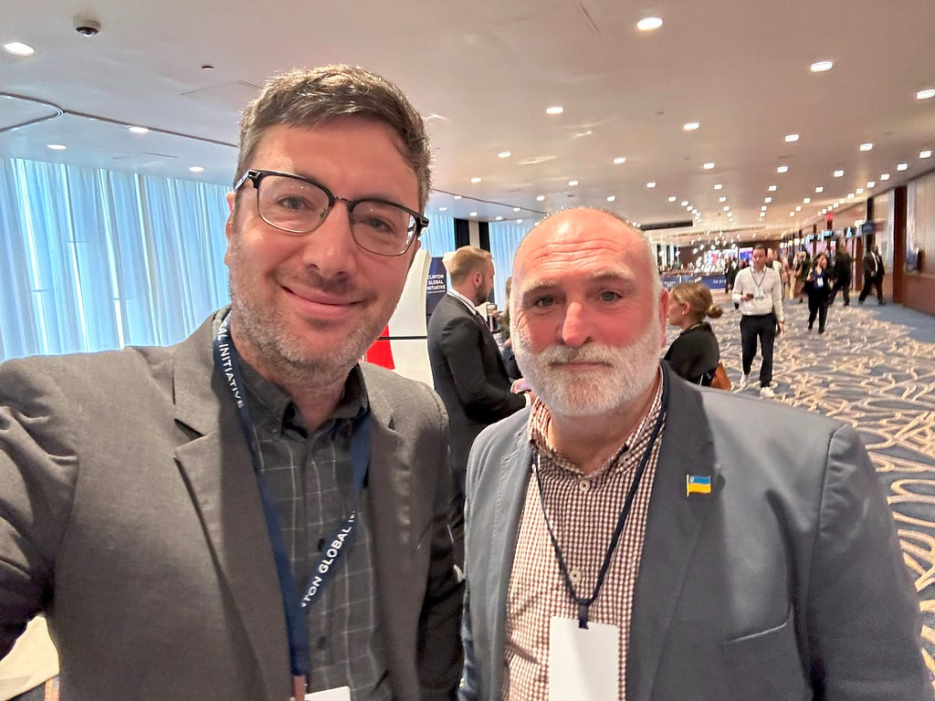 Joe and Chef Jose Andres smile at the camera at CGI23. They are wearing gray jackets.