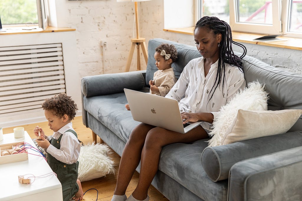 Woman in White long sleeve shirt sitting on grey couch using a computer with 2 kids | Awesome Websites For Content Writers: Work From Home | Money, Freelance, Work from home, make money from home, Medium
