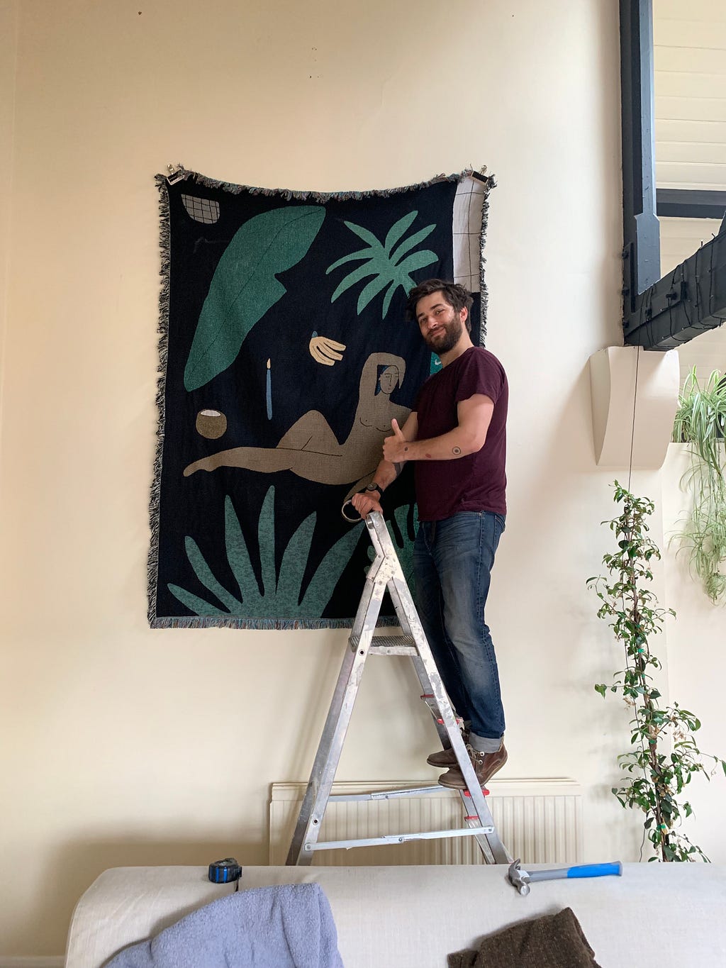 The author stood on a ladder looking very pleased with himself after hanging a large tapestry wall hanging.