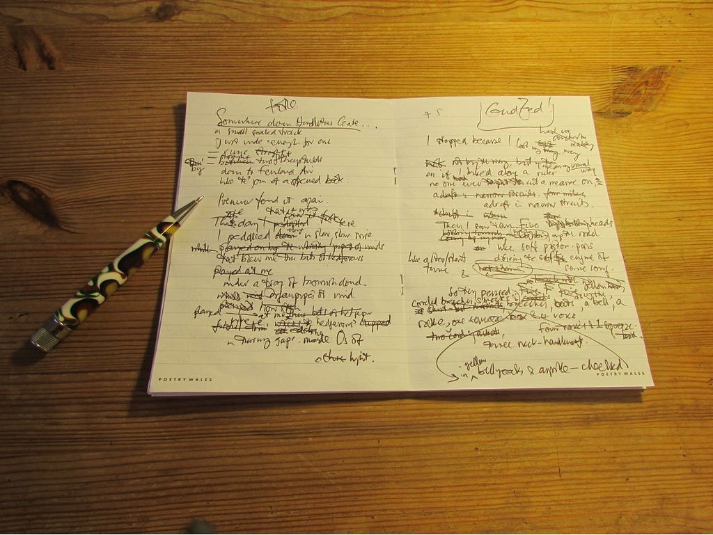 Photograph of handwritten poem in black ink on white paper, and a black, white and yellow pen on a wooden table.