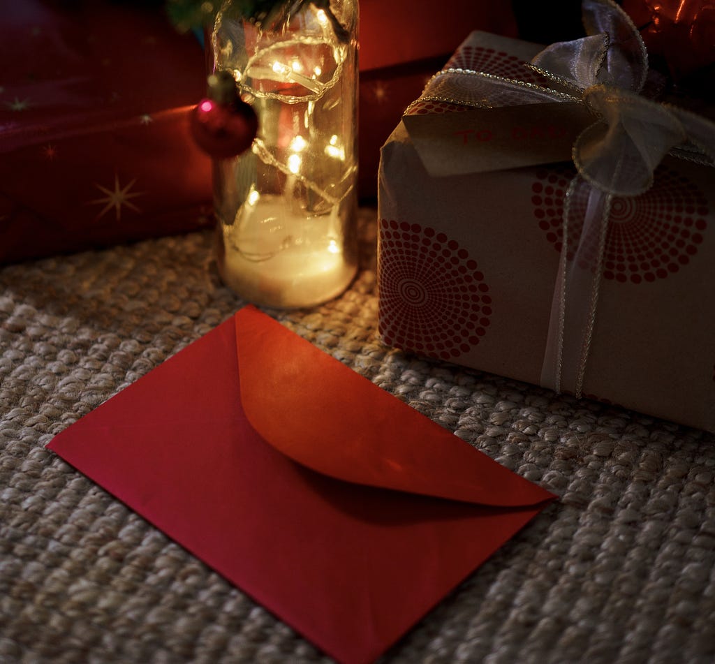 Red envelope on table with gift and lighted bottle. Christmas bulb hanging on bottle.